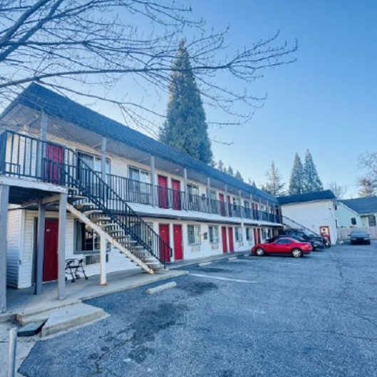 Two-story Stagecoach Motel with red doors, an exterior staircase and balcony beside a parking area.